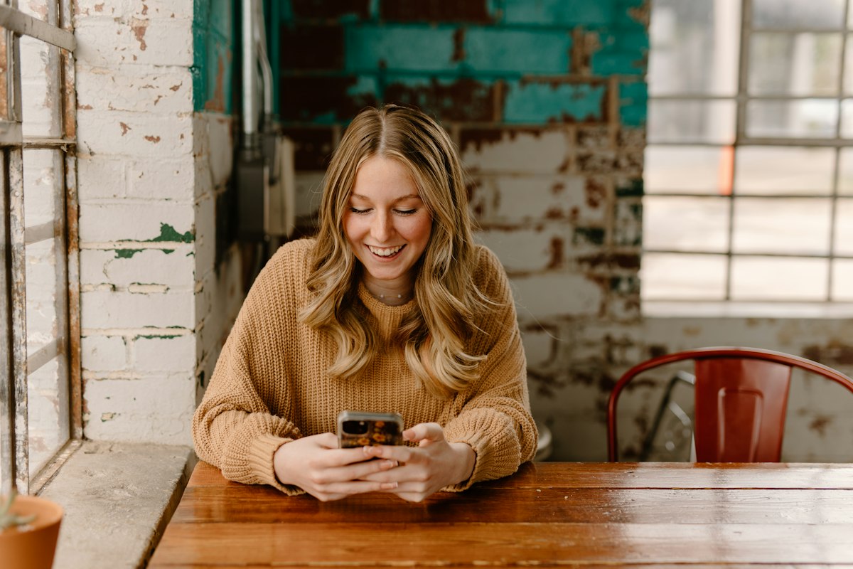 Mulher sentada à mesa olhando o celular, ilustrando a Visão geral criada por IA do Google